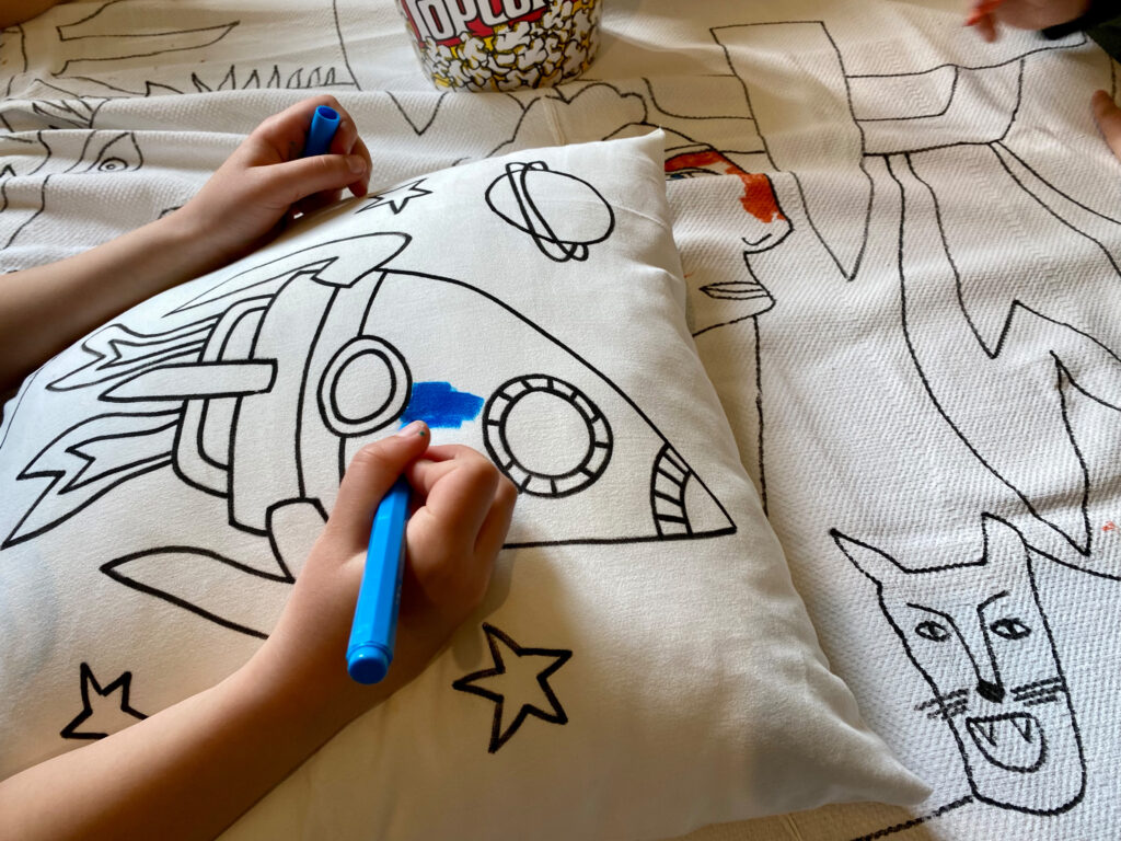 Piccole manine colorano la federa di un cuscino con i pennarelli