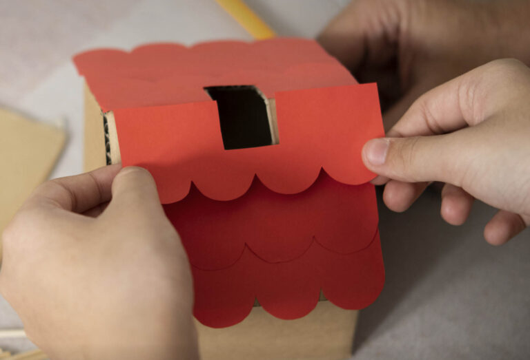mani di bambino con in mano del cartone rosso durante il laboratorio di riciclo del cartone
