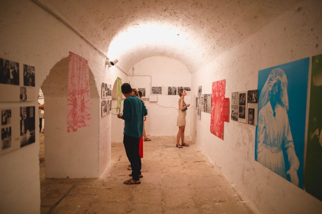 visitatori che guardano i quadri della mostra sul tarantismo nella sala della tabaccaia